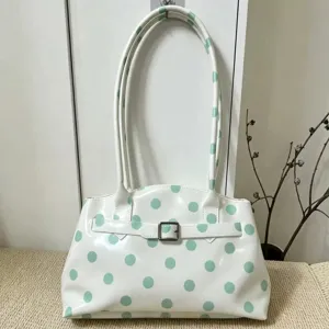Dettaglio di una borsa a tracolla in PVC bianco a pois verde menta con fibbia argentata