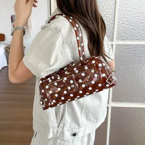 Stylish brown polka dot PVC underarm bag with glossy finish shown being worn by a model