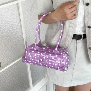 Detailed view of a trendy purple polka dot PVC jelly underarm bag held by a model.
