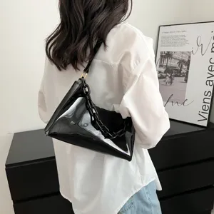 Back view of a woman carrying a black glossy patent leather underarm bag with a chunky chain