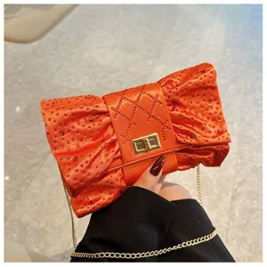Élégante pochette de soirée orange avec nœud en strass et chaîne en métal doré.