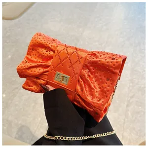 Vue détaillée de la pochette de soirée orange à nœud avec strass et chaîne d'or.