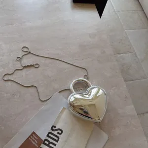 Silver heart-shaped acrylic evening bag featuring metallic finish and long chain strap