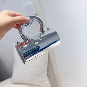 Mini silver metallic evening bag featuring a unique heart handle and cylindrical body design.