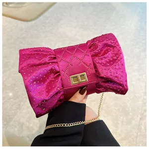 Élégante pochette de soirée fuchsia en forme de nœud avec strass et chaîne dorée.