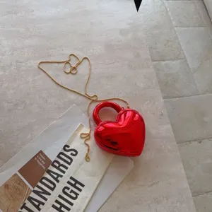 Macro view of metallic red heart-shaped acrylic evening bag with gold chain detail