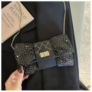 Gros plan d'une pochette de soirée en velours noir en forme de nœud avec strass dorés.