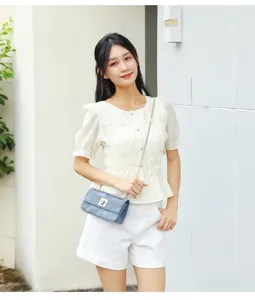 Elegante signora in bianco con una borsa a tracolla retrò in denim blu e catena