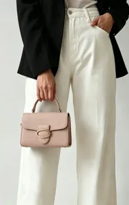 Close-up of an elegant dusty pink pebbled leather handbag featuring a gold oval clasp