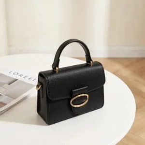 Elegant minimalist black leather top-handle bag with gold oval buckle on white round table.