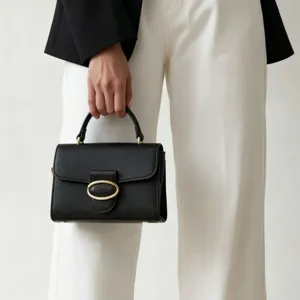 Elegant black textured leather handbag featuring a gold oval buckle held by a model