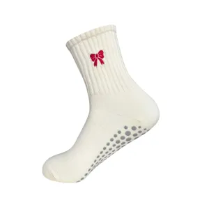 Detalle de calcetines de yoga blancos con bordado de lazo rojo y puntos antideslizantes.