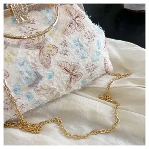 Nahaufnahme einer Abendtasche mit Schmetterlingsstickerei, Diamantverschluss und goldener Kette