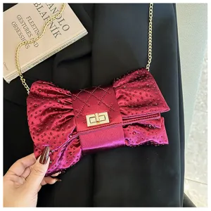 Gros plan d'une pochette élégante bordeaux en forme de nœud avec strass et chaîne dorée.
