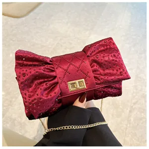 Détail d'une pochette de soirée bordeaux en forme de nœud avec strass et chaîne d'or.