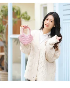 Dettaglio di una borsa a mano rosa a forma di cuore trapuntata, tenuta da una modella.