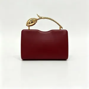 Detail of elegant burgundy evening clutch bag with creative golden rose handle.