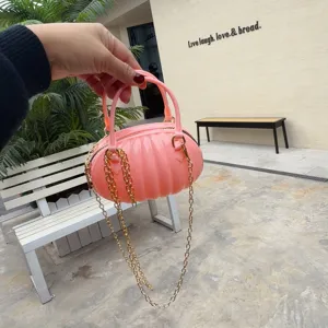 Détail d'un sac à main rose en PVC en forme de citrouille avec chaîne dorée tenu à la main.