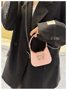 Detail view of a pink bow jelly bag with gold chain strap on model in black blazer.