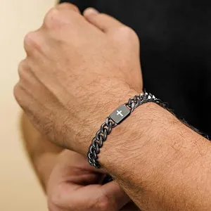 Close-up of a black stainless steel Cuban link bracelet with a cross plate on a man's wrist