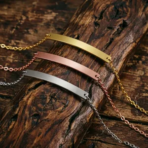 Set of three stainless steel bar bracelets in gold, rose gold, and silver on rustic wood.