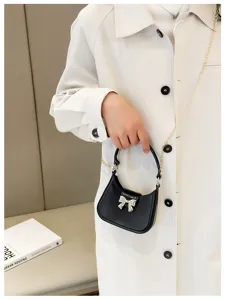 Close-up of black jelly bag with silver bow detail and gold chain strap held by hand.