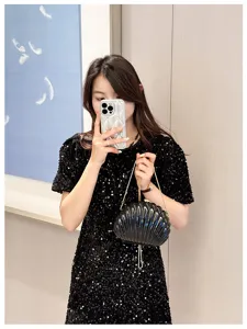 Elegant black shell-shaped chain clutch bag held by a model wearing a sequined dress