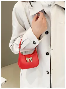 Stylish red PVC jelly underarm handbag with a golden bow detail and beige coat