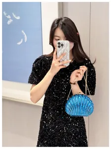 Elegant blue shell-shaped evening clutch bag with gold chain strap carried by model