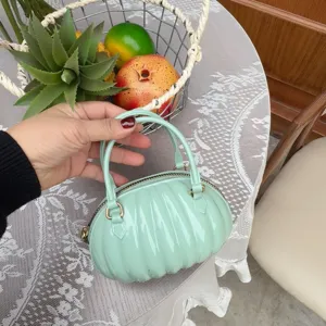 Gros plan d'un mini sac à main en PVC vert menthe en forme de citrouille tenu à la main.