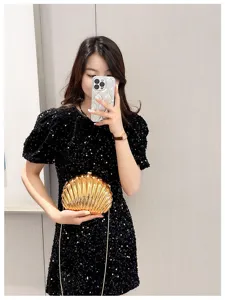 Close-up view of a stylish golden shell-shaped evening clutch bag with chain held by a model