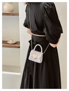 Mini white PVC jelly bag with heart lock and gold chain strap worn as a crossbody bag