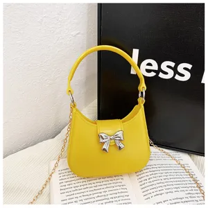 Macro view of vibrant yellow jelly handbag featuring a metallic silver bow and chain strap.