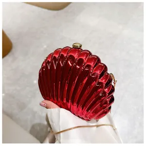 Elegant shiny red shell-shaped evening clutch bag held in hand with metallic finish