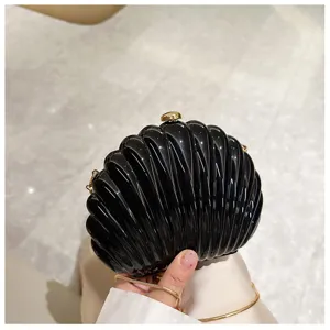 Detailed view of a gloss black shell-shaped evening bag with a gold metal chain strap