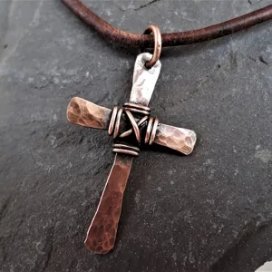 Nahaufnahme eines rustikalen handgefertigten Kupferkreuzanhängers mit Hammerschlag-Textur.