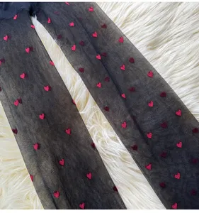Close-up of black sheer pantyhose featuring cute red heart patterns, ultra-thin design detail.