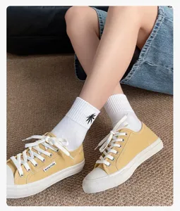 Stylish women's yellow canvas shoes paired with white crew socks and black leaf embroidery.