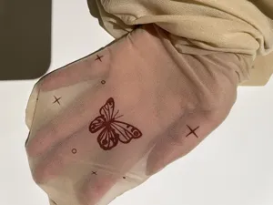 Close-up detail of sheer nude mesh fabric with red butterfly tattoo print, soft stretchy.