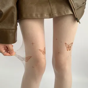Close-up detail of sheer nude tights featuring delicate butterfly and star tattoo prints.