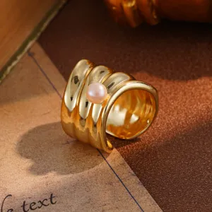 Macro view of a chunky gold-toned wave-textured ring featuring a single pink pearl