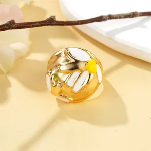 Détail d'une bague dorée texturée avec des motifs de fleurs en émail blanc et jaune.