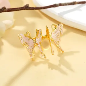 Détail d'une bague ouverte dorée ornée de deux papillons en émail rose clair avec texture.