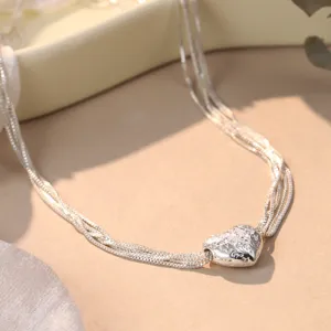 Detailed macro view of a silver heart pendant necklace with intricate embossed floral patterns