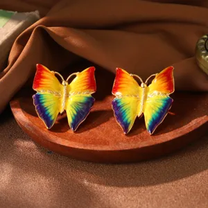 Detailansicht von farbenfrohen Regenbogen-Emaille-Schmetterlingsohrsteckern auf Holztablett.