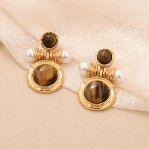 Détail rapproché de boucles d'oreilles rétro dorées avec pierres œil de tigre et perles blanches