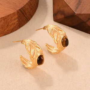 Macro view of vintage C-shaped gold earrings with feather texture and tiger eye stone.