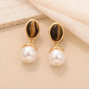 Détail macro de boucles d'oreilles rétro oeil de tigre brun et perle blanche, or