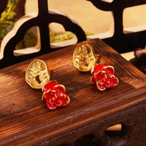 Détail de boucles d'oreilles fleur en émail rouge et papillon doré sur support en bois