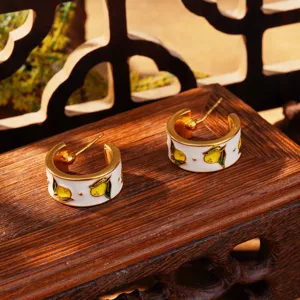 Gros plan de créoles en émail de style chinois avec motif de fruits jaunes.